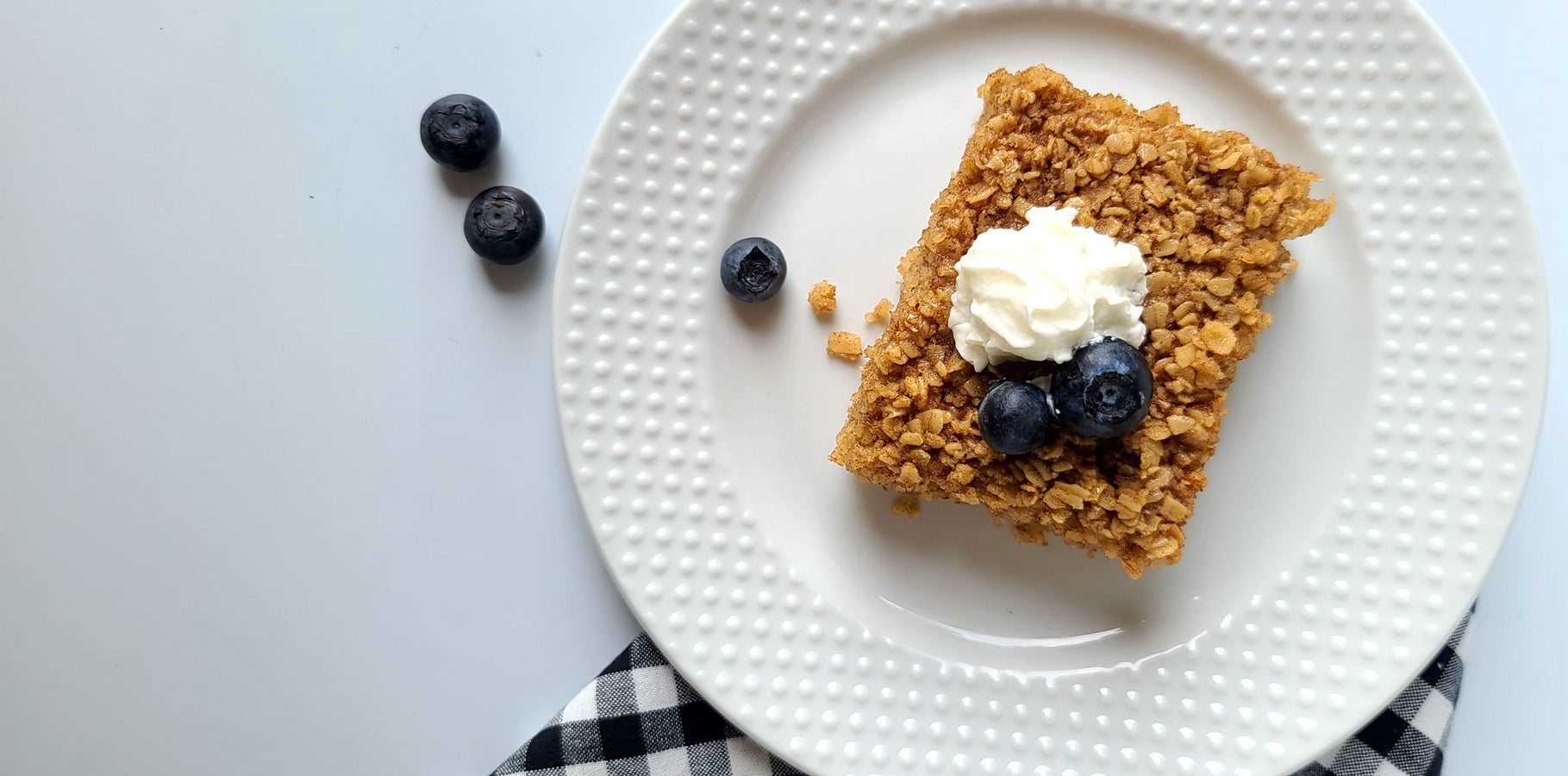 Slice of baked oatmeal with whipped cream and blueberries on a white plate