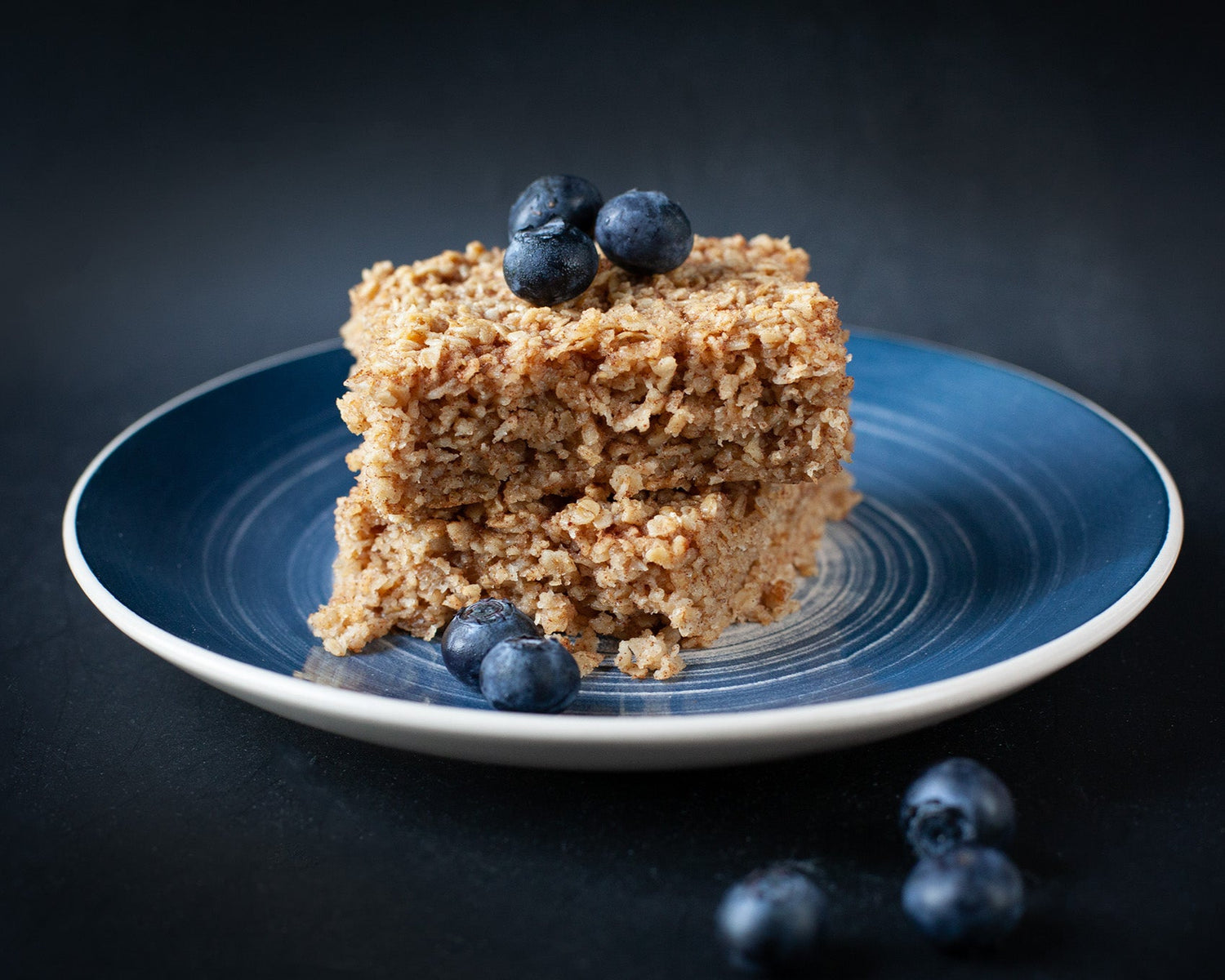 Baked oatmeal bars with blueberries on a blue plate against a dark background